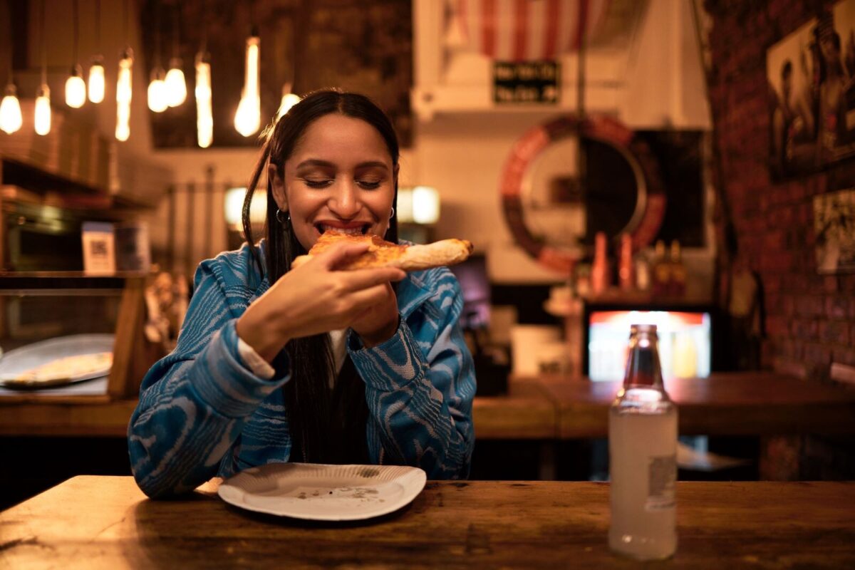 woman eating a slice of pizza in a dimly lit restaurant