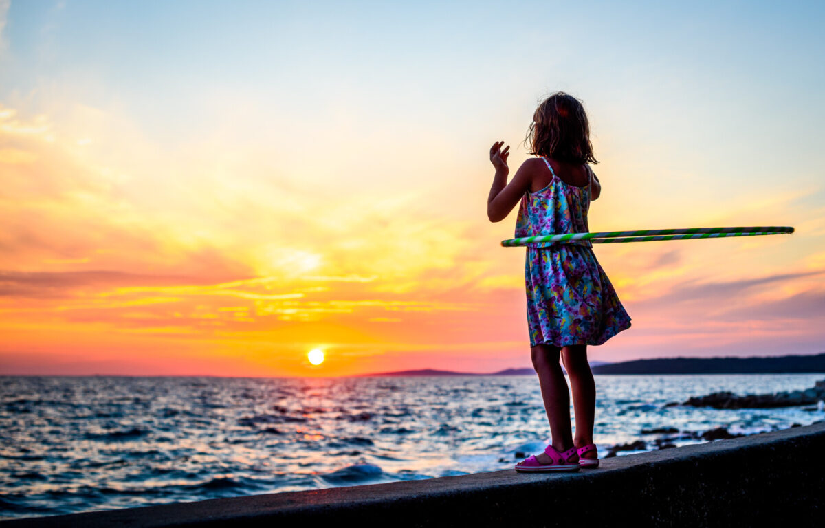 young girl hula hooping in front of sunset