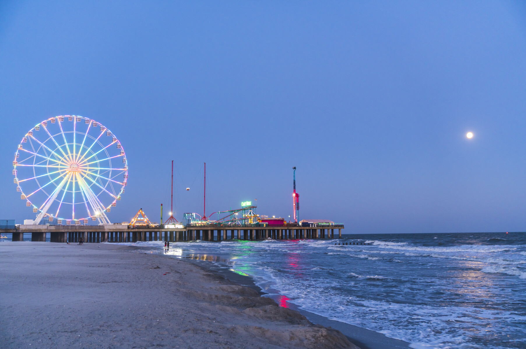 A beautiful twilight view of the iconic Steel Pier in Atlantic City, featuring the illuminated Ferris wheel reflecting on the ocean waves. This vibrant boardwalk destination offers world-class entertainment and excitement for guests staying at nearby Long & Foster Vacation Rentals properties.